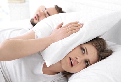 Woman covering ear with pillow due to man’s snoring in Covington, GA