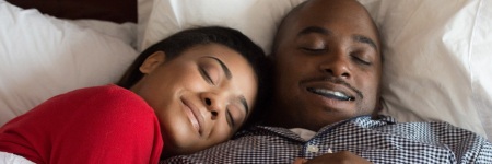 Man with sleep apnea appliance and woman sleeping soundly