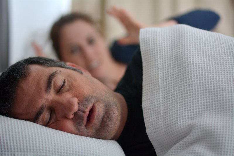 Man on side snoring, irritated wife in background