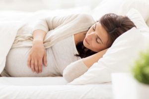 Pregnant woman sleeping between white sheets